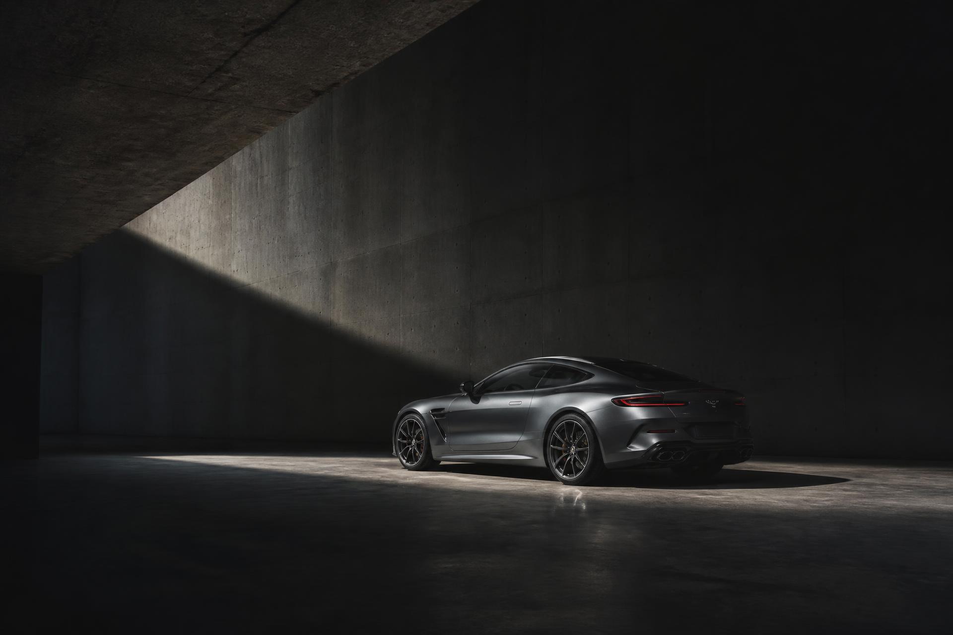 A silver German performance coupé standing in a dark concrete hall, lit by a single shaft of light